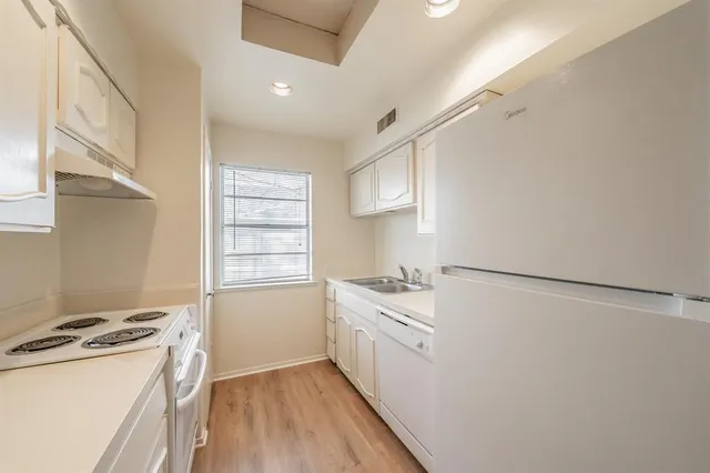 a kitchen with stainless steel appliances granite countertop a sink a refrigerator and white cabinets with wooden floor