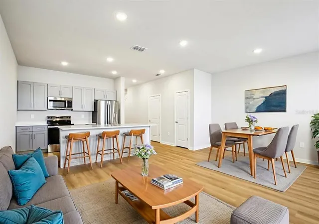 a living room with stainless steel appliances kitchen island granite countertop a couch and a dining table with wooden floor