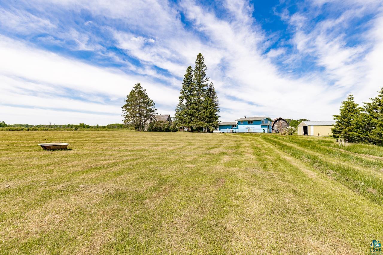 6606 Metso Road Kettle River, MN 55757 - Photo 61 of 84 Expansive green space featuring multiple structures, including a blue residential building, a large barn, and a yellow outbuilding