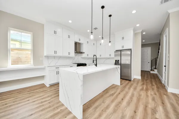 a large white kitchen with stainless steel appliances kitchen island granite countertop a refrigerator and a sink