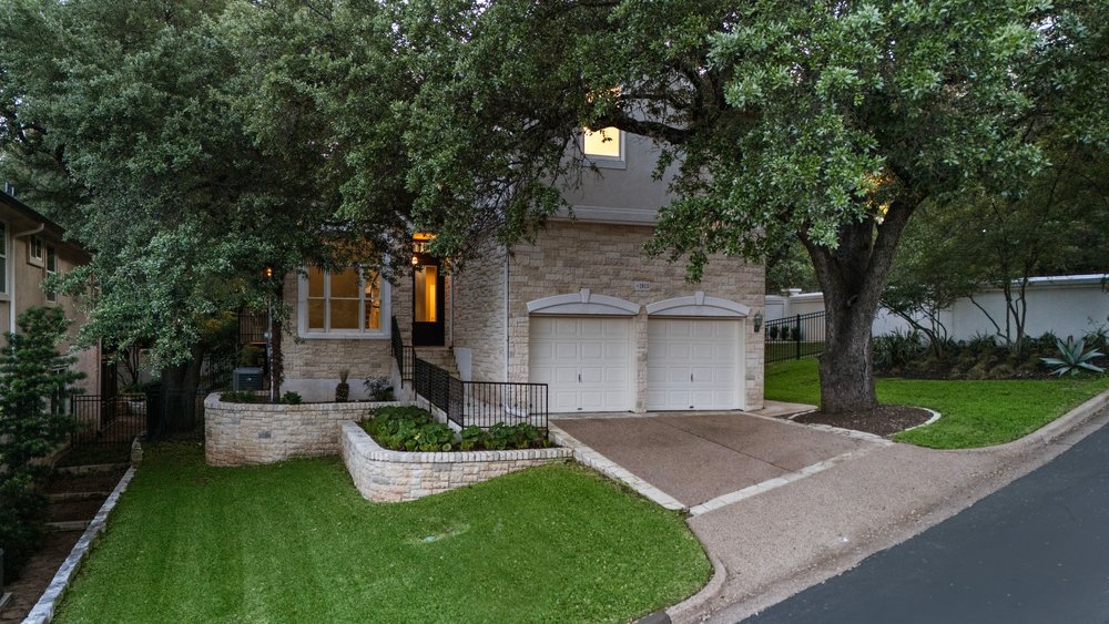 1815 Rue De St Tropez Austin, TX 78746 - Photo 16 of 40 Stone exterior with a two-car garage, mature trees, tiered landscaping, and a paved driveway