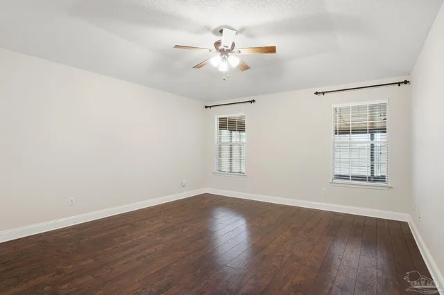 an empty room with wooden floor chandelier fan and windows