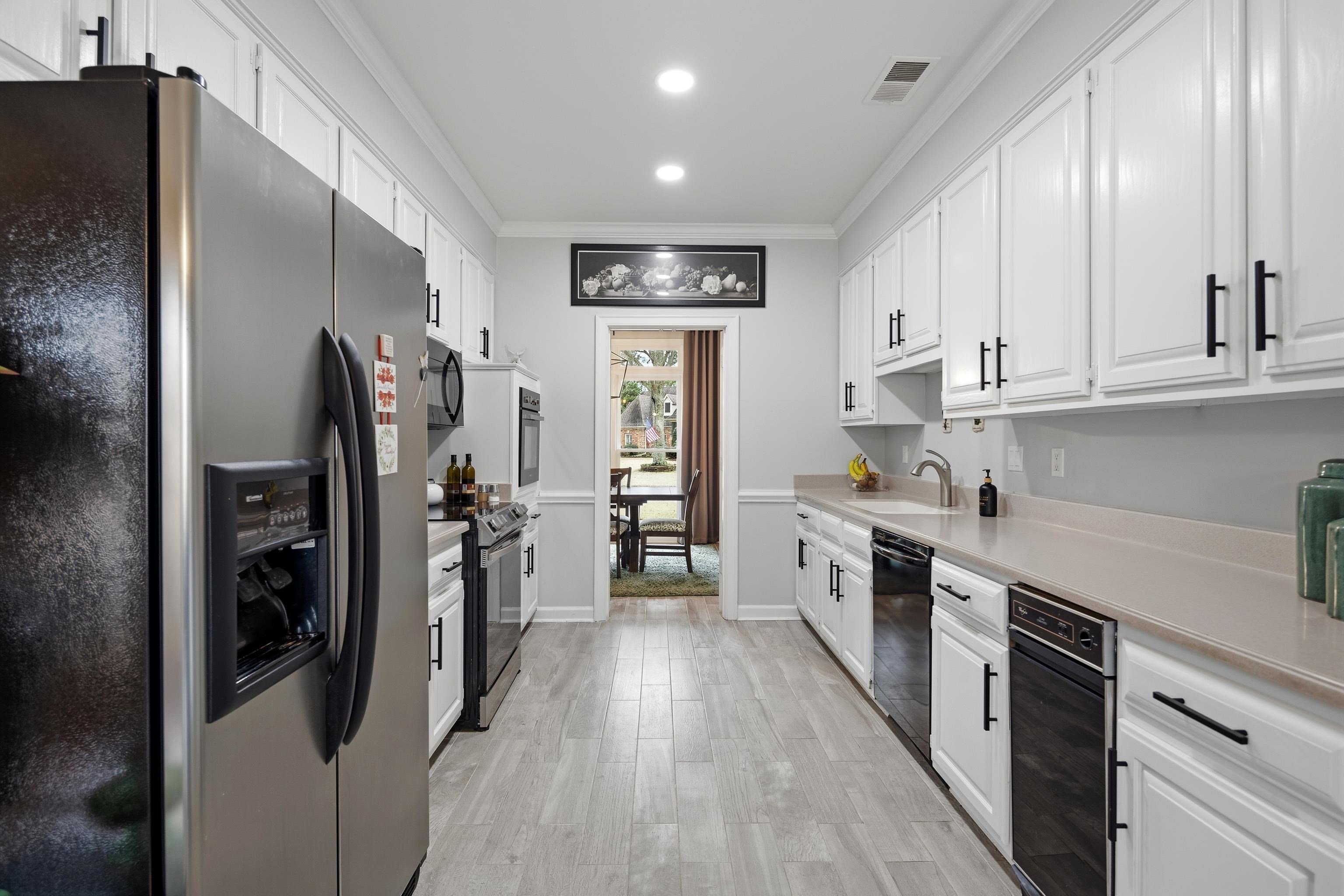 10281 Peyton Path Cove Collierville, TN 38017 - Photo 36 of 40 Kitchen with black appliances, white cabinetry, light countertops, crown molding, and light wood finished floors