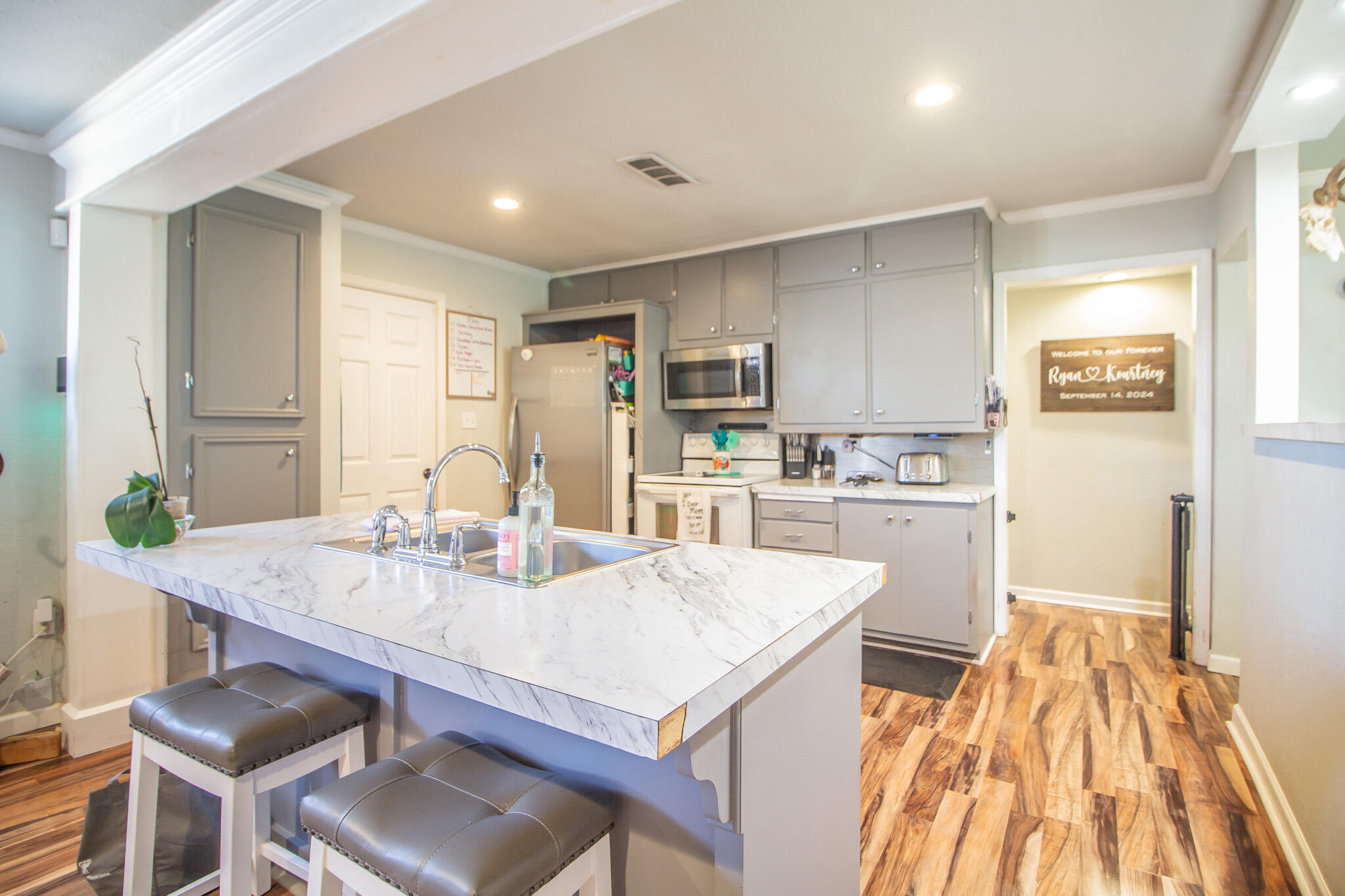 6403 23rd Street Lubbock, TX 79407 - Photo 7 of 29 a open kitchen with kitchen island a stove a sink dishwasher and white cabinets with wooden floor
