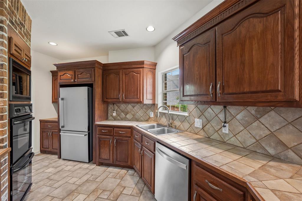 5607 Ranger Drive Rockwall, TX 75032 - Photo 18 of 40 Kitchen featuring rich wood cabinetry with decorative molding, stainless steel appliances, tile countertops, tile backsplash, and recessed lighting