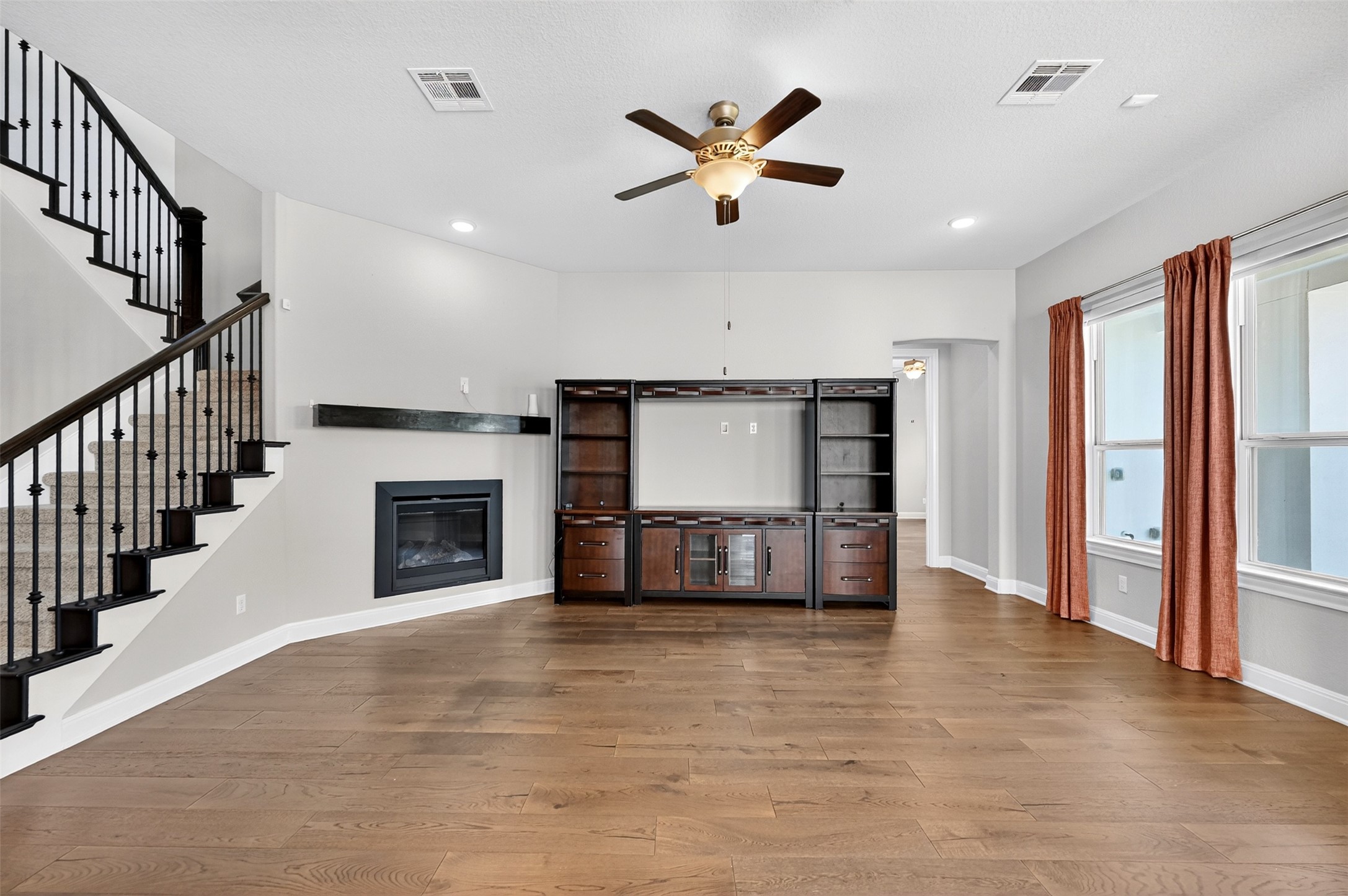 1201 Positano Pass Leander, TX 78641 - Photo 19 of 40 Spacious living area featuring wood-finish flooring, a built-in media center, an electric fireplace with a floating mantel, and a staircase with wrought iron balusters