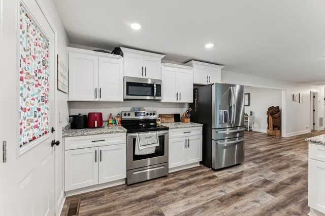 a kitchen with stainless steel appliances a stove a sink a refrigerator white cabinets and wooden floor