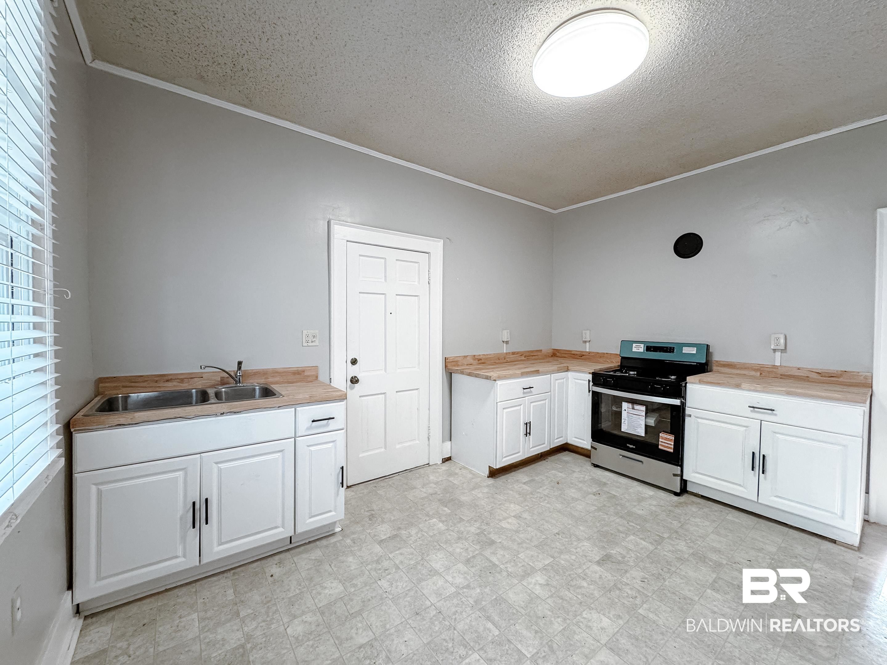 206 1st Street Mobile, AL 36611 - Photo 11 of 26 Kitchen with white cabinets, stainless steel gas range, ornamental molding, a textured ceiling, and light floors