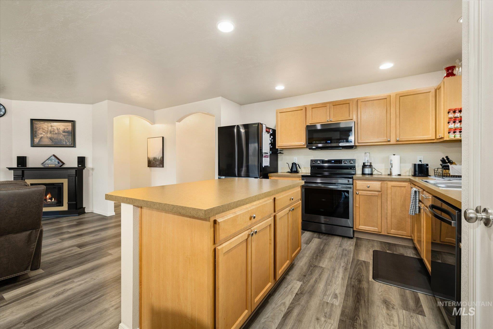 7166 Yellow Fern Road Nampa, ID 83687 - Photo 35 of 35 Kitchen with black appliances, a kitchen island, open floor plan, dark wood finished floors, and a warm lit fireplace