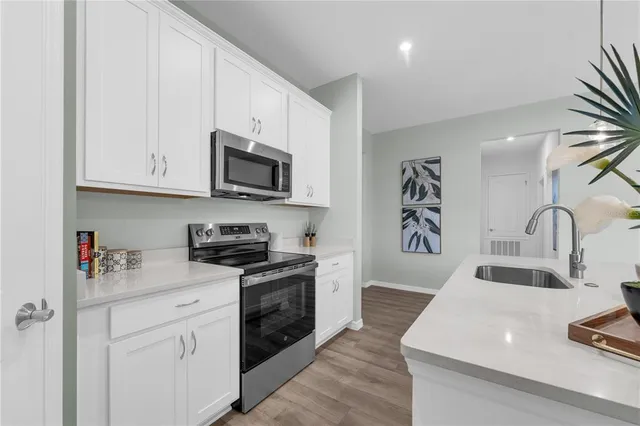 a kitchen with stainless steel appliances granite countertop a sink dishwasher stove and white cabinets with wooden floor