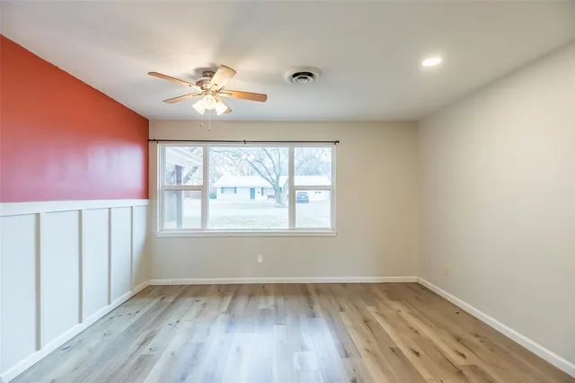an empty room with wooden floor chandelier fan and windows
