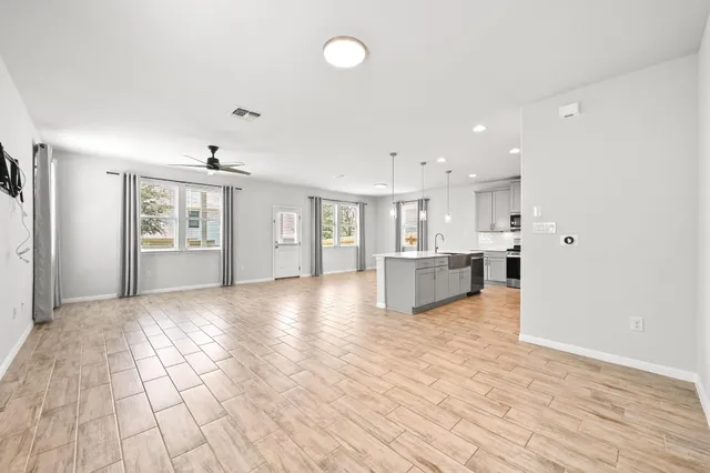 a view of an empty room and kitchen with wooden floor