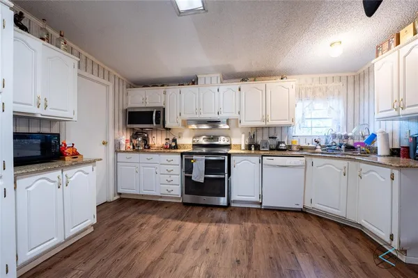 a kitchen with granite countertop wooden floors stainless steel appliances a sink and cabinets
