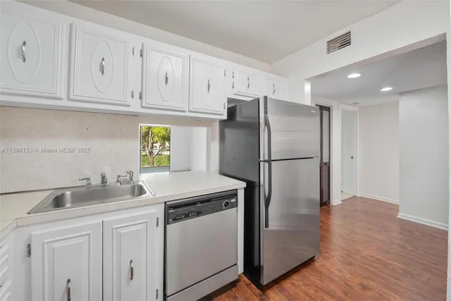 a kitchen with stainless steel appliances granite countertop a refrigerator a sink a stove and white cabinets with wooden floors