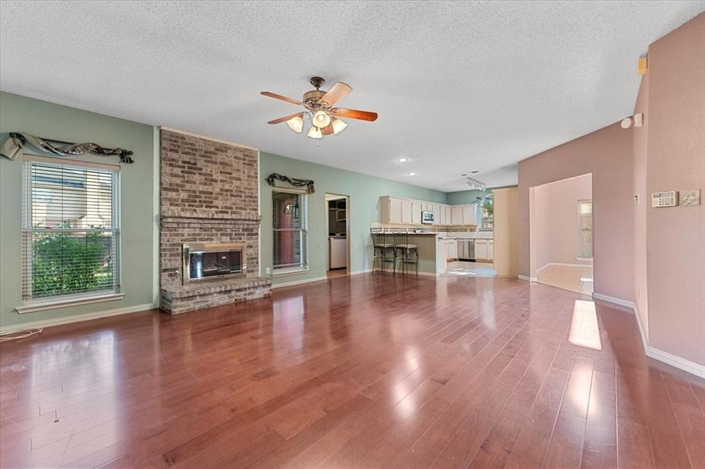6752 MacIntosh Drive Plano, TX 75023 - Photo 2 of 40 Unfurnished living room with a fireplace, dark wood-type flooring, a textured ceiling, and a ceiling fan