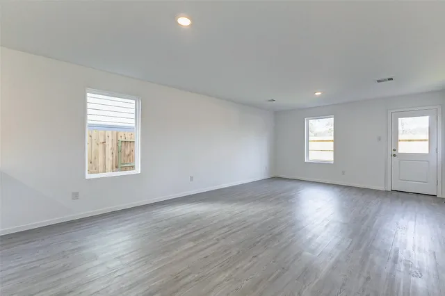 a view of an empty room with wooden floor and window