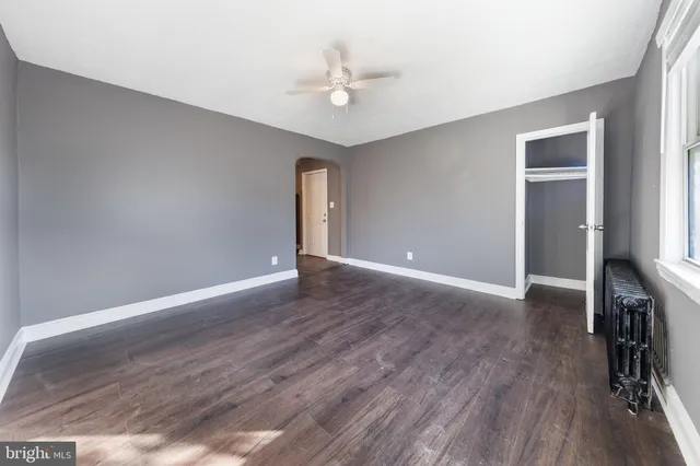 a view of an empty room with wooden floor and a ceiling fan