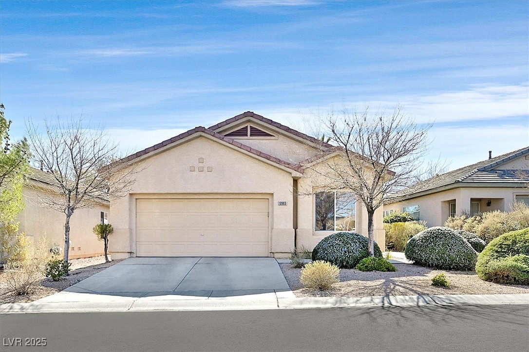 Single story home featuring a garage, concrete driveway, a tile roof, and stucco siding