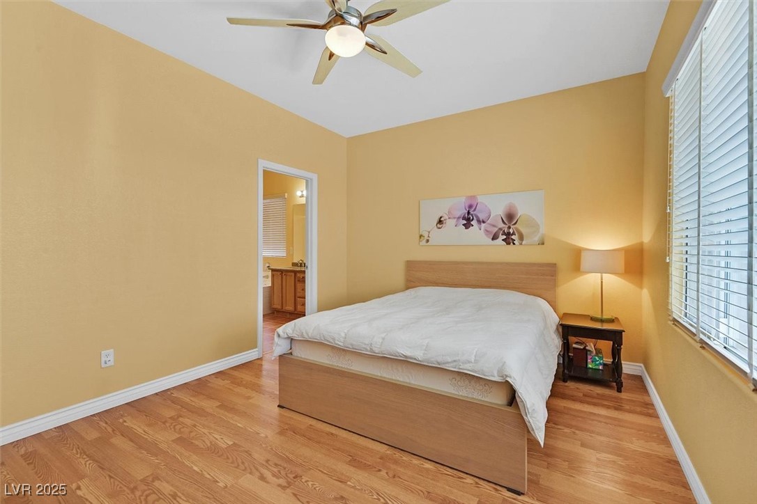 10983 Pumpkin Ridge Avenue Las Vegas, NV 89135 - Photo 16 of 35 Bedroom featuring baseboards, connected bathroom, a ceiling fan, and light wood-style floors