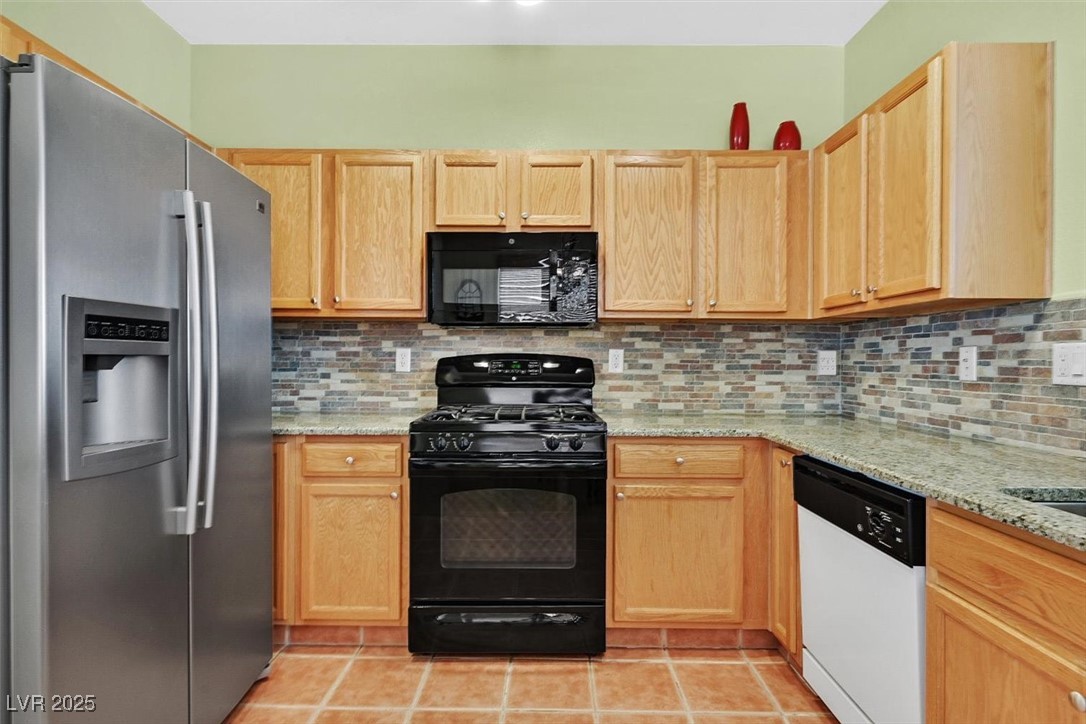 10983 Pumpkin Ridge Avenue Las Vegas, NV 89135 - Photo 8 of 35 Kitchen with black appliances, light stone counters, backsplash, and light brown cabinetry