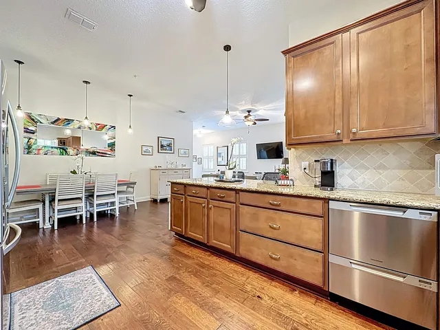 a kitchen with stainless steel appliances granite countertop a stove top oven a sink a dining table and chairs with wooden floor