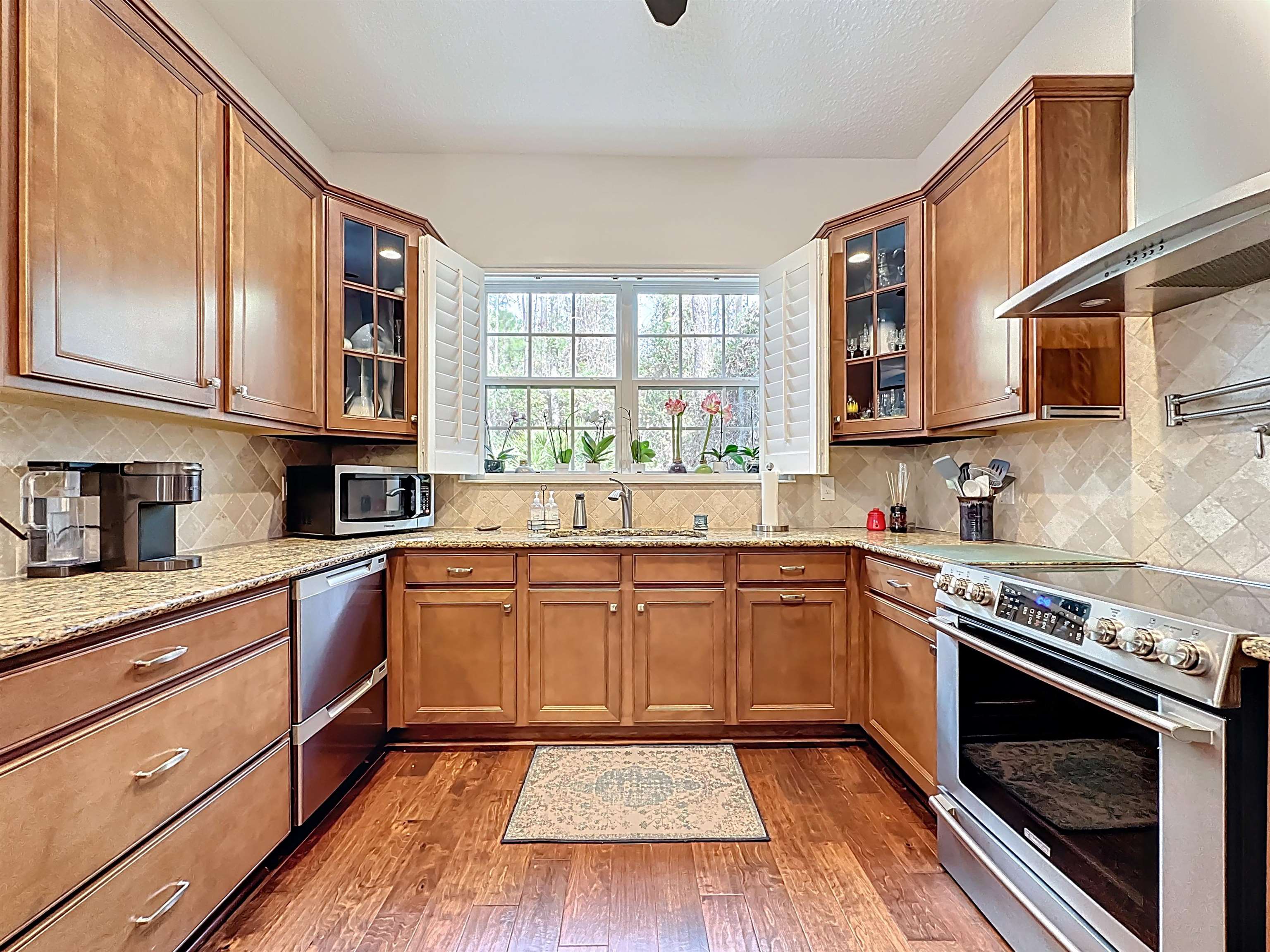 130 Grand Ravine Drive St. Augustine, FL 32086 - Photo 13 of 42 Kitchen with appliances with stainless steel finishes, wall chimney range hood, glass insert cabinets, and brown cabinetry