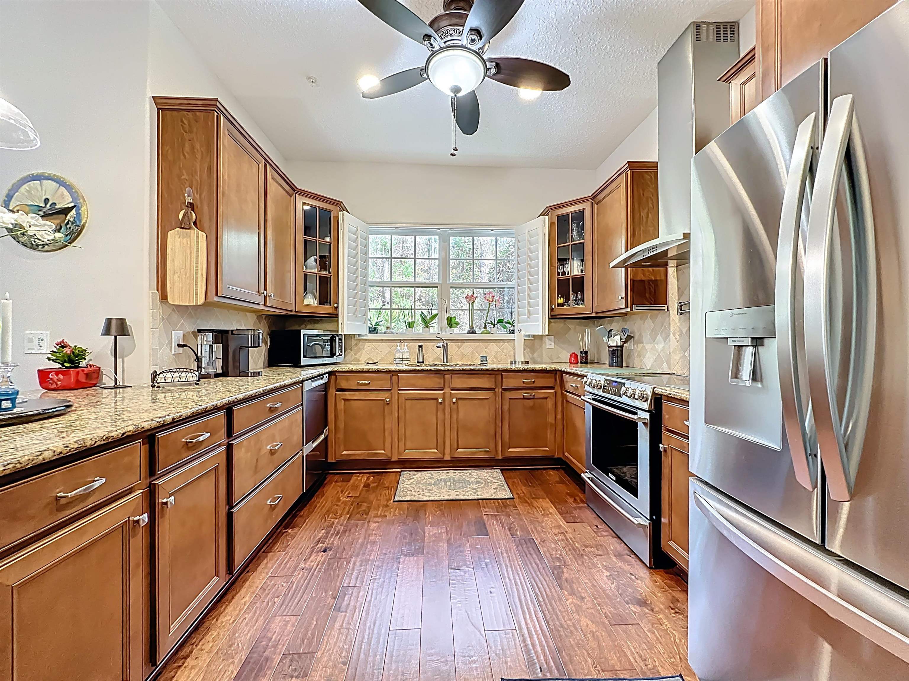 130 Grand Ravine Drive St. Augustine, FL 32086 - Photo 9 of 42 Kitchen featuring appliances with stainless steel finishes, brown cabinetry, glass insert cabinets, wall chimney range hood, and a textured ceiling