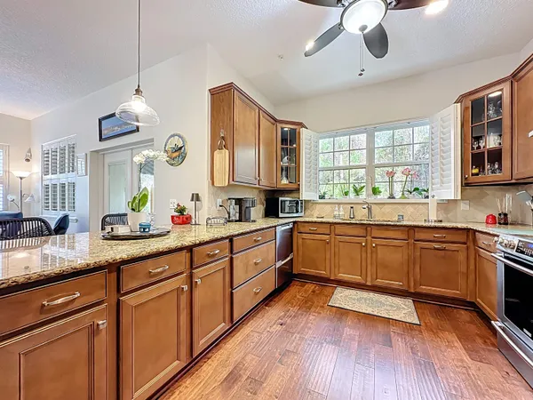 a kitchen with stainless steel appliances granite countertop a stove top oven a sink a dining table and chairs with wooden floor