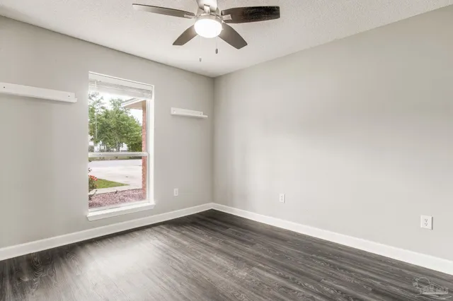 an empty room with wooden floor fan and windows
