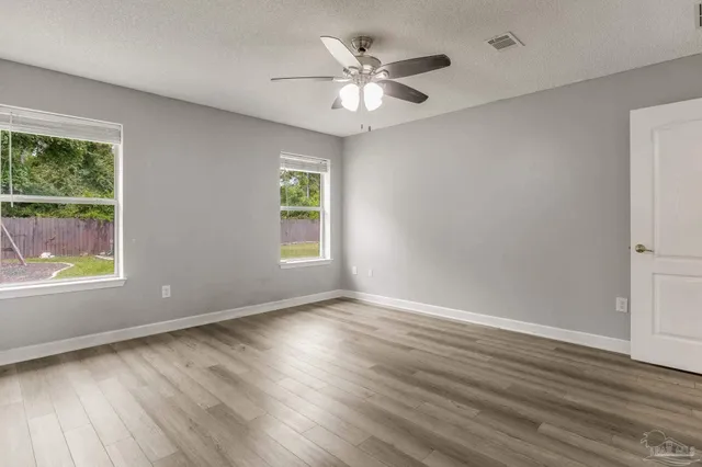 an empty room with wooden floor chandelier fan and windows