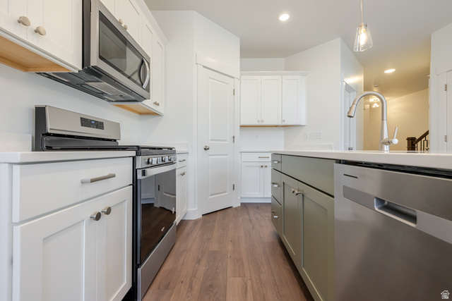 4816 Heartwood Road, Unit 423 Mapleton, UT 84664 - Photo 9 of 21 Dual tone kitchen featuring stainless steel appliances, two tone cabinetry, dark wood finished floors, pendant lighting, and light stone counters