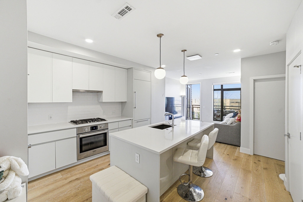 191 Washington Street, Unit 413 Boston, MA 02135 - Photo 25 of 40 a large white kitchen with a stove a sink dishwasher and a refrigerator with wooden floor