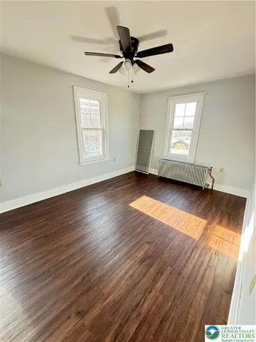 an empty room with wooden floor fan and windows