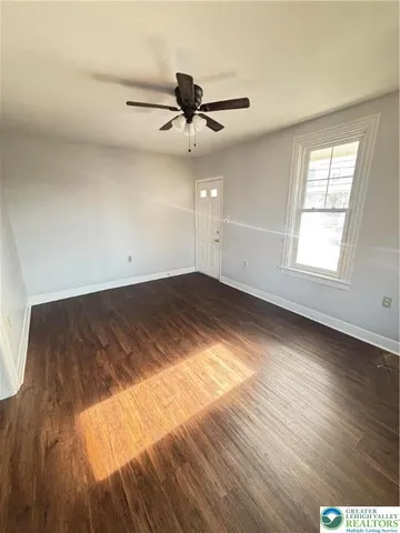an empty room with wooden floor fan and windows