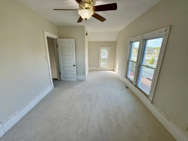 an empty room with chandelier fan and windows
