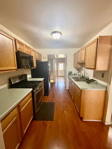 a kitchen with stainless steel appliances granite countertop a stove a sink a refrigerator white cabinets and wooden floor