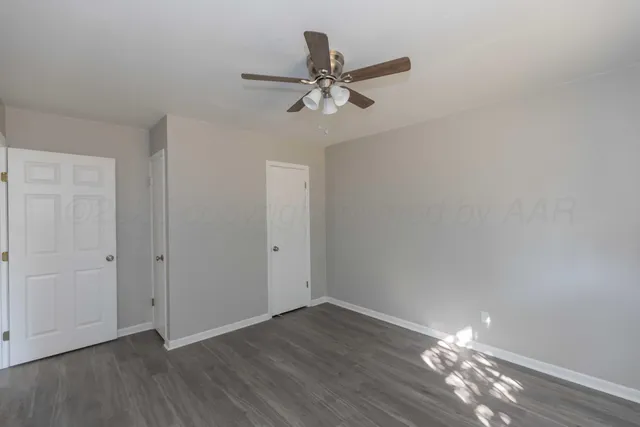 a view of an empty room with wooden floor and a ceiling fan
