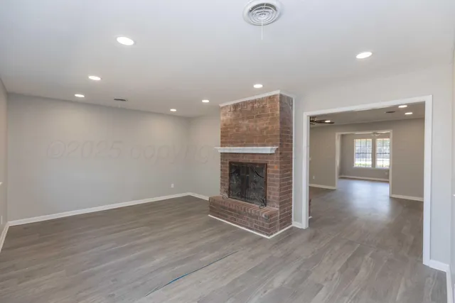 an empty room with wooden floor fireplace and windows