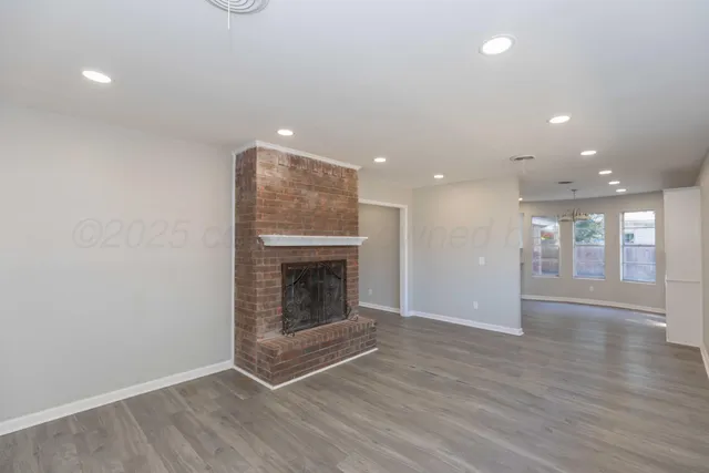 an empty room with wooden floor fireplace and windows