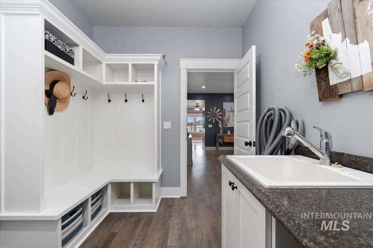 15015 Leon Lane Caldwell, ID 83607 - Photo 17 of 44 Mudroom featuring custom white built-in storage with coat hooks and cubbies, wood-finish flooring, a utility sink with a dark speckled countertop, and white shaker-style cabinetry