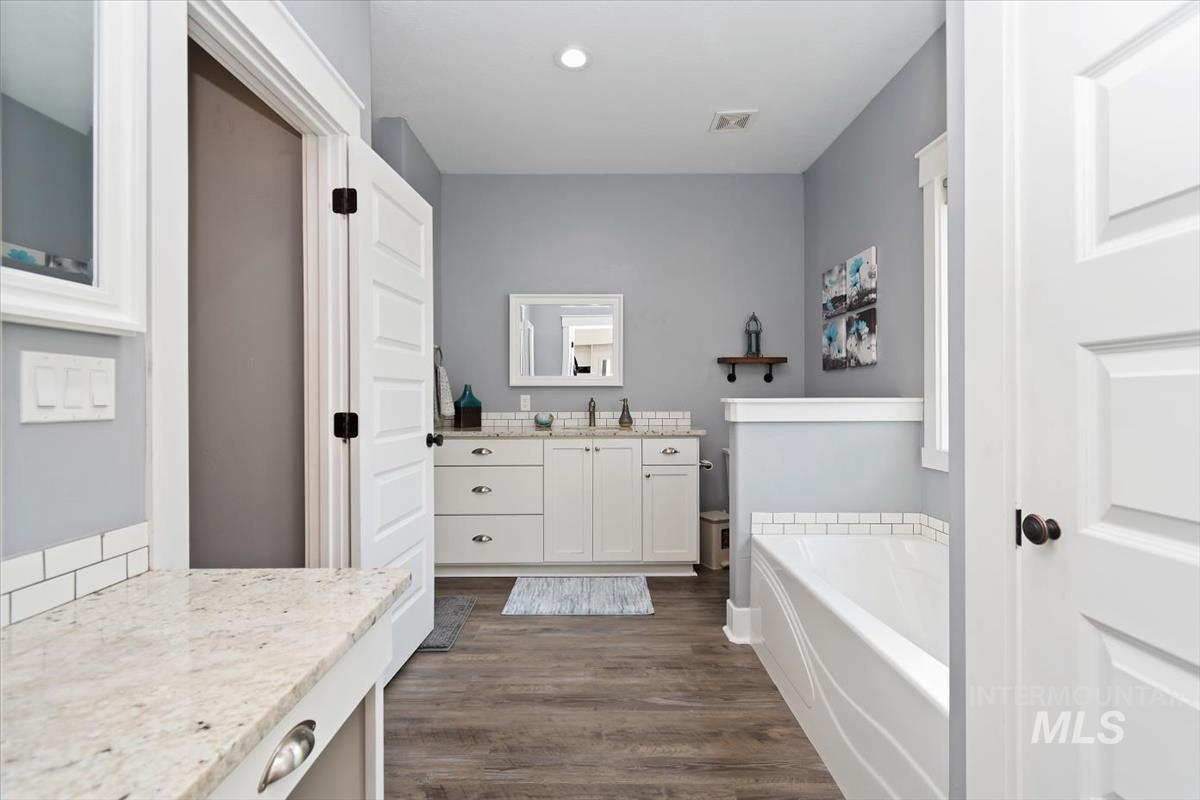 15015 Leon Lane Caldwell, ID 83607 - Photo 21 of 44 Bathroom featuring a white double vanity with light-toned countertops, a built-in tub with subway tile surround, wood-finish flooring, and white trim