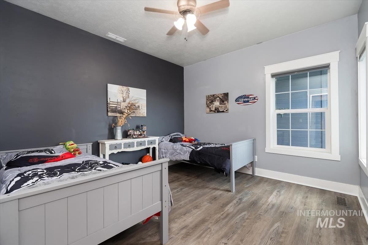 15015 Leon Lane Caldwell, ID 83607 - Photo 29 of 44 Spacious bedroom featuring wood-finish flooring, a ceiling fan with light fixture, and a large window with white trim