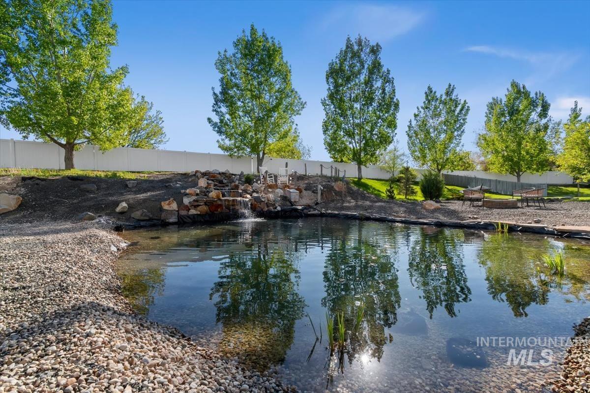 15015 Leon Lane Caldwell, ID 83607 - Photo 3 of 44 Serene backyard pond featuring a rock waterfall, gravel shoreline, and mature trees