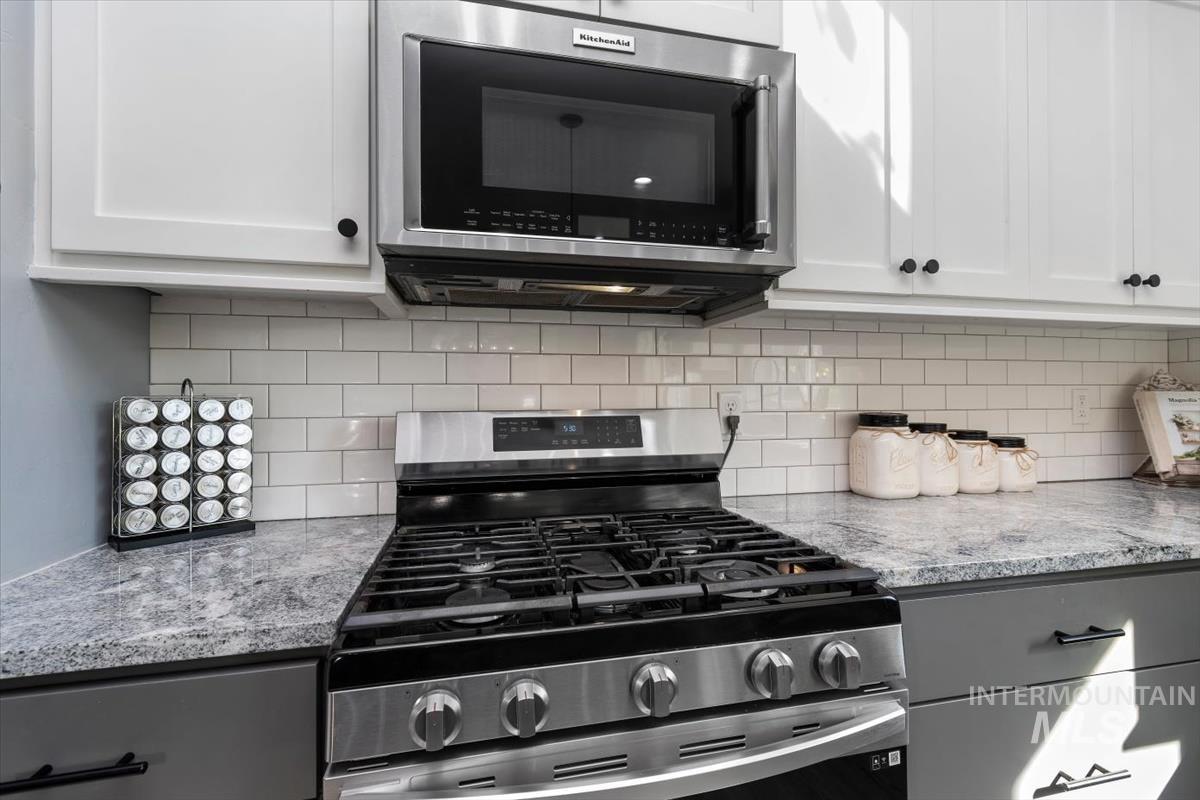 15015 Leon Lane Caldwell, ID 83607 - Photo 10 of 44 Stainless steel gas range with coordinating microwave oven, white subway tile backsplash, light-toned countertops, and two-tone cabinetry with matte black hardware