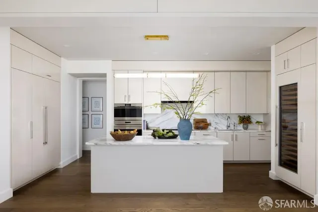 a white kitchen with stainless steel appliances a stove a refrigerator a sink and white cabinets with wooden floor