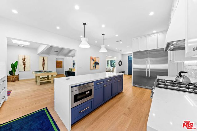 a large kitchen with stainless steel appliances kitchen island a large counter top a stove a chimney a sink and a refrigerator