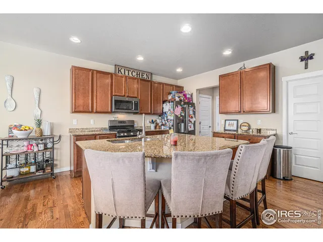 a kitchen with stainless steel appliances granite countertop a stove top oven a sink a dining table and chairs with wooden floor