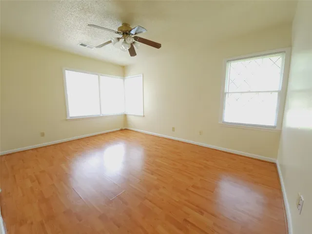an empty room with wooden floor chandelier fan and windows