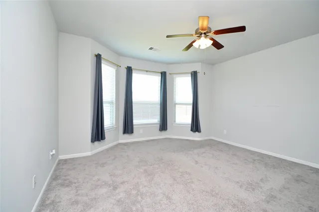 an empty room with chandelier fan and windows