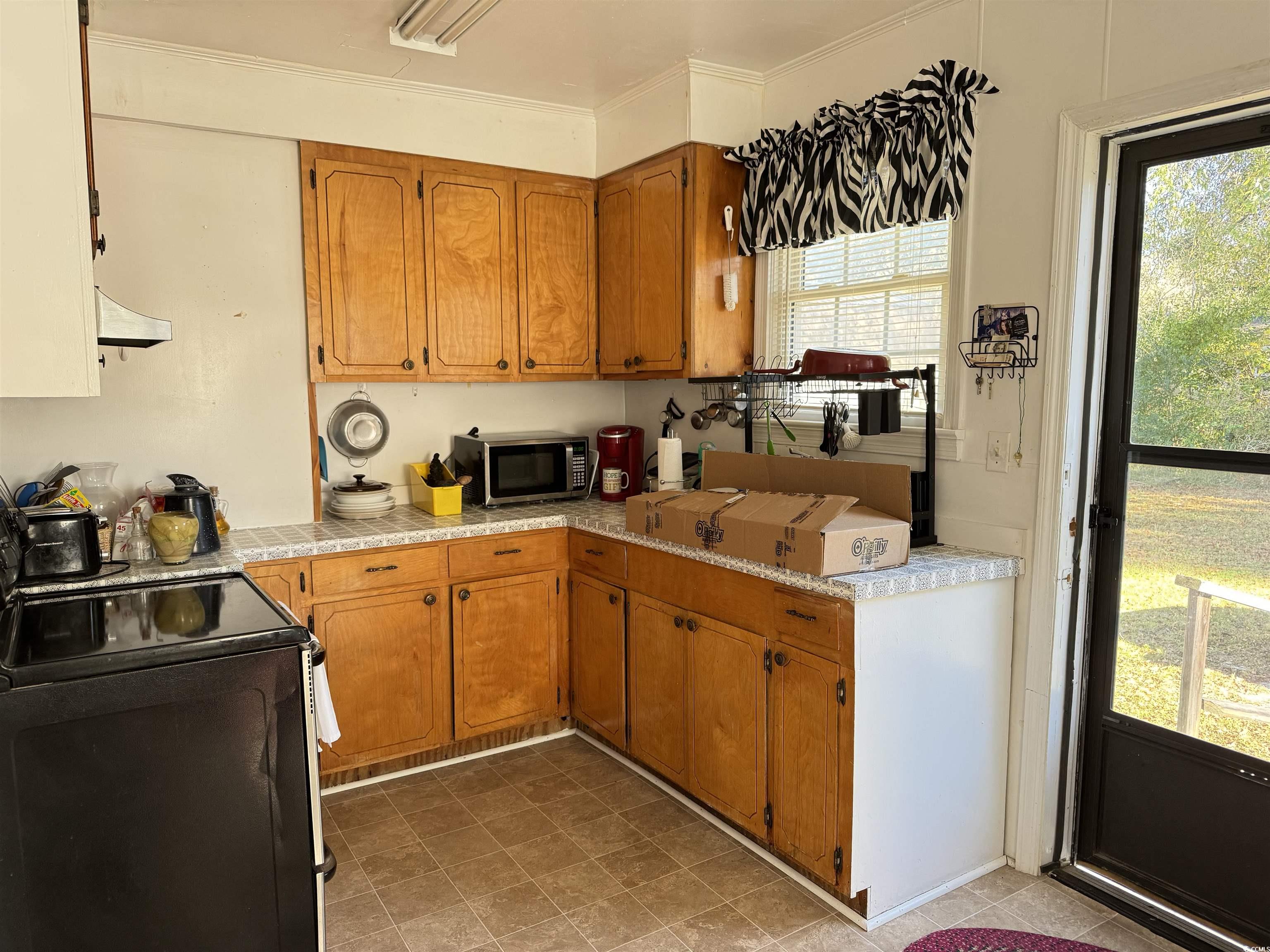 4206 Stevens Street Loris, SC 29569 - Photo 3 of 10 Kitchen with brown cabinets, light countertops, electric range, stainless steel microwave, and crown molding
